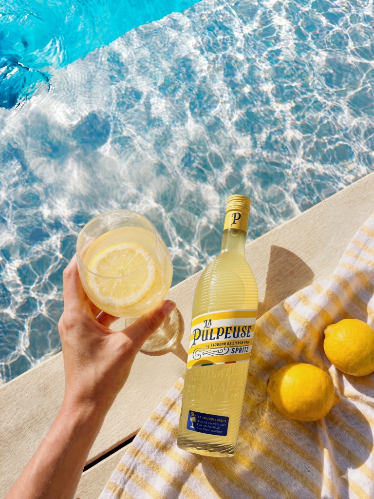 Bouteille La Pulpeuse Spritz, citron et verre au bord de la piscine